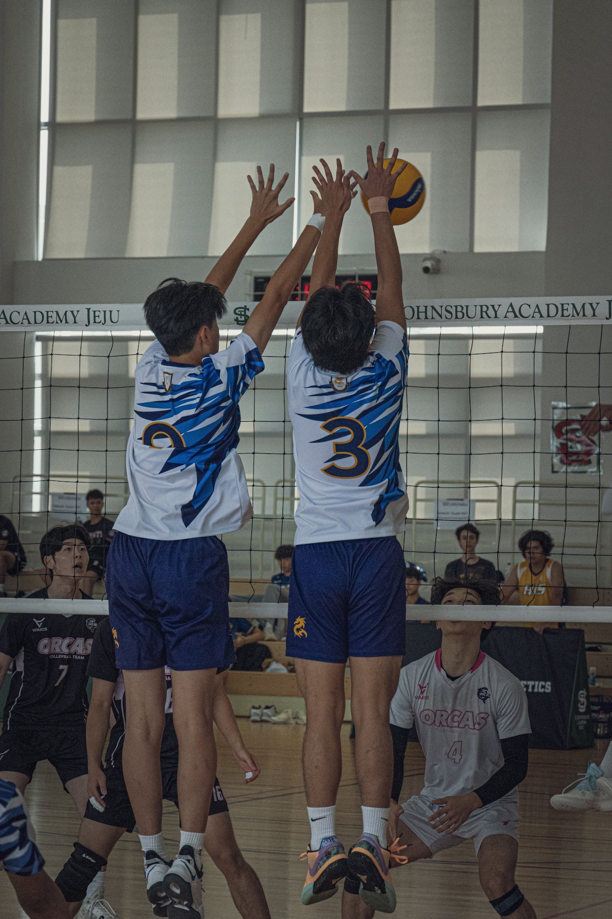 Two blockers in white jerseys go up together at the net